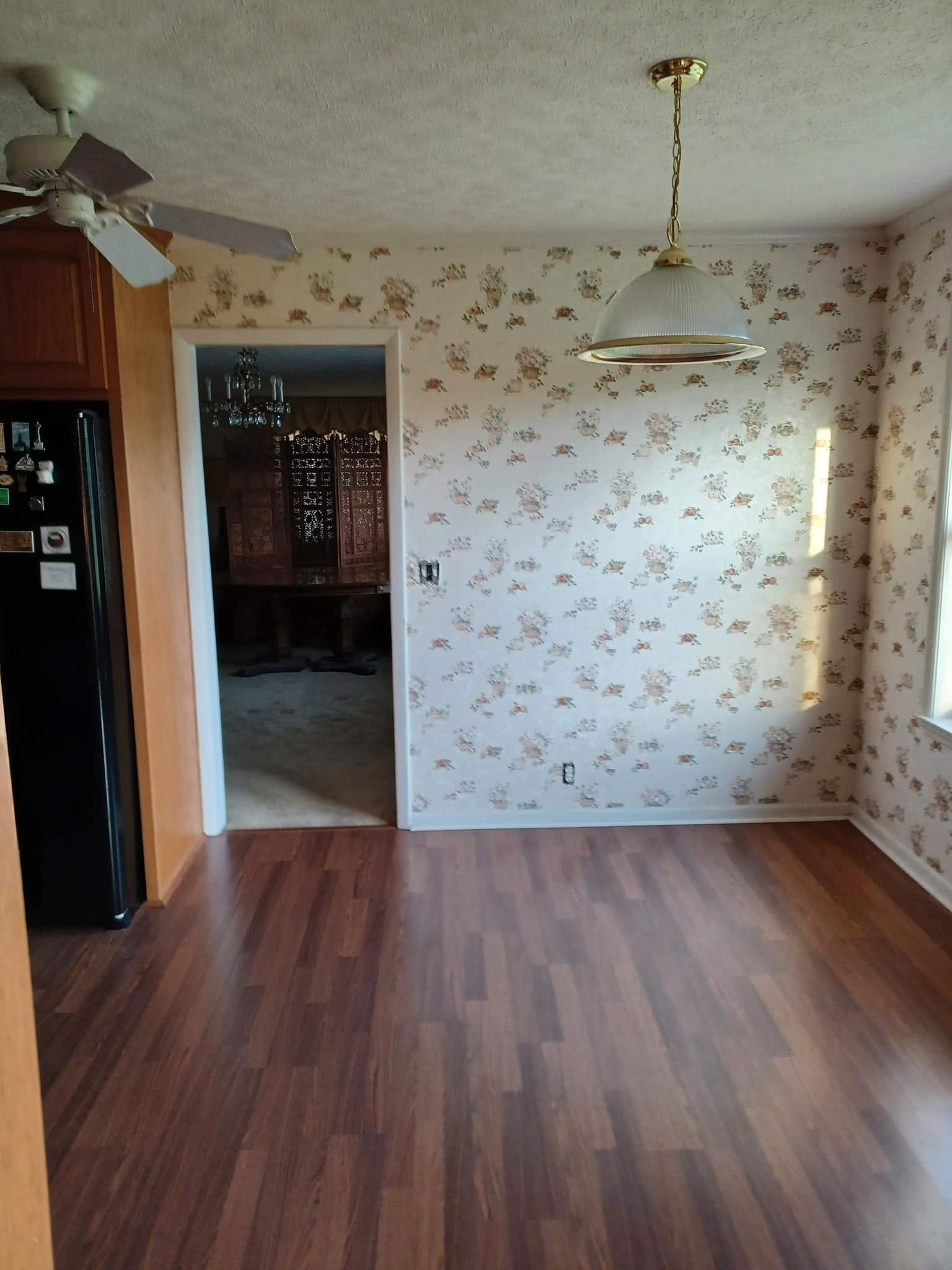 A brightly lit dining area with wood-look laminate flooring, floral wallpaper, and a pendant lamp hanging over the center of the room.