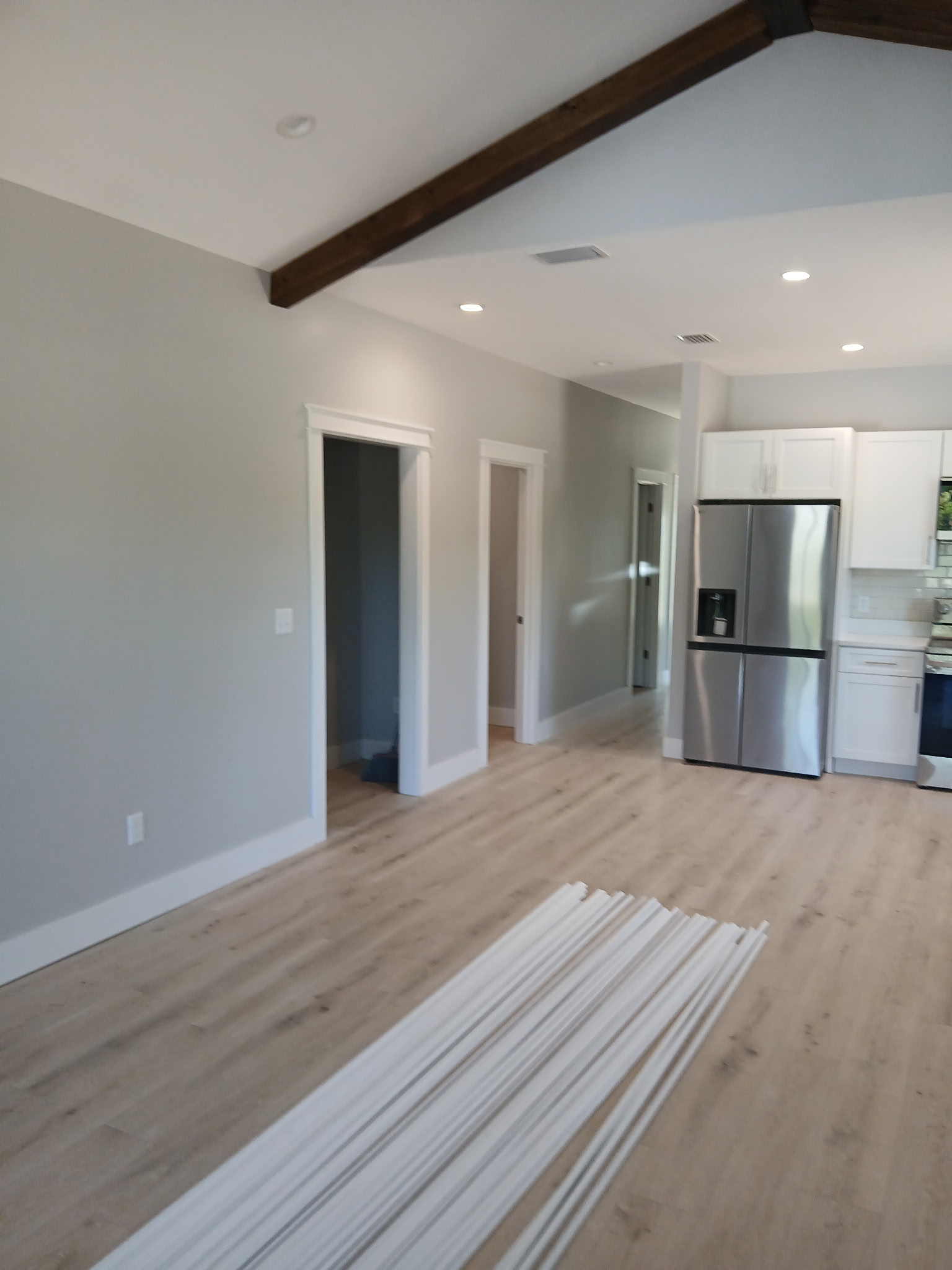 Bright, modern open-plan kitchen and living area with gray walls, wood floors, exposed beam, stainless refrigerator, and white trim.